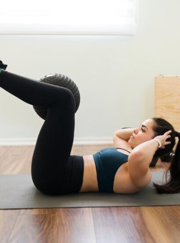 side-view-determined-young-woman-holding-slam-ball-with-her-legs-doing-abdominal-crunches-have-flat-abs_662251-1367